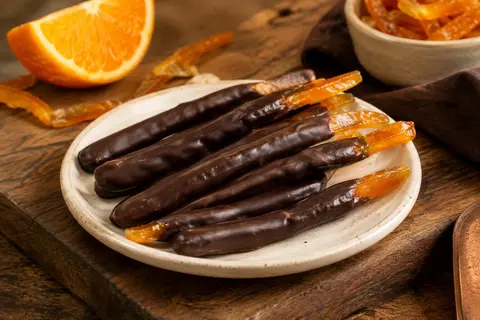 Bâtonnets d’écorce d’orange confite enrobés de chocolat noir présentés sur une assiette en céramique